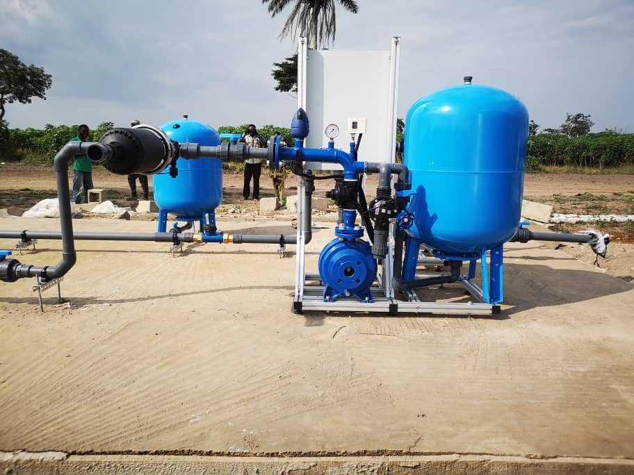 A blue electric pump set with two pressure tanks and a disc filter on a concrete pad.