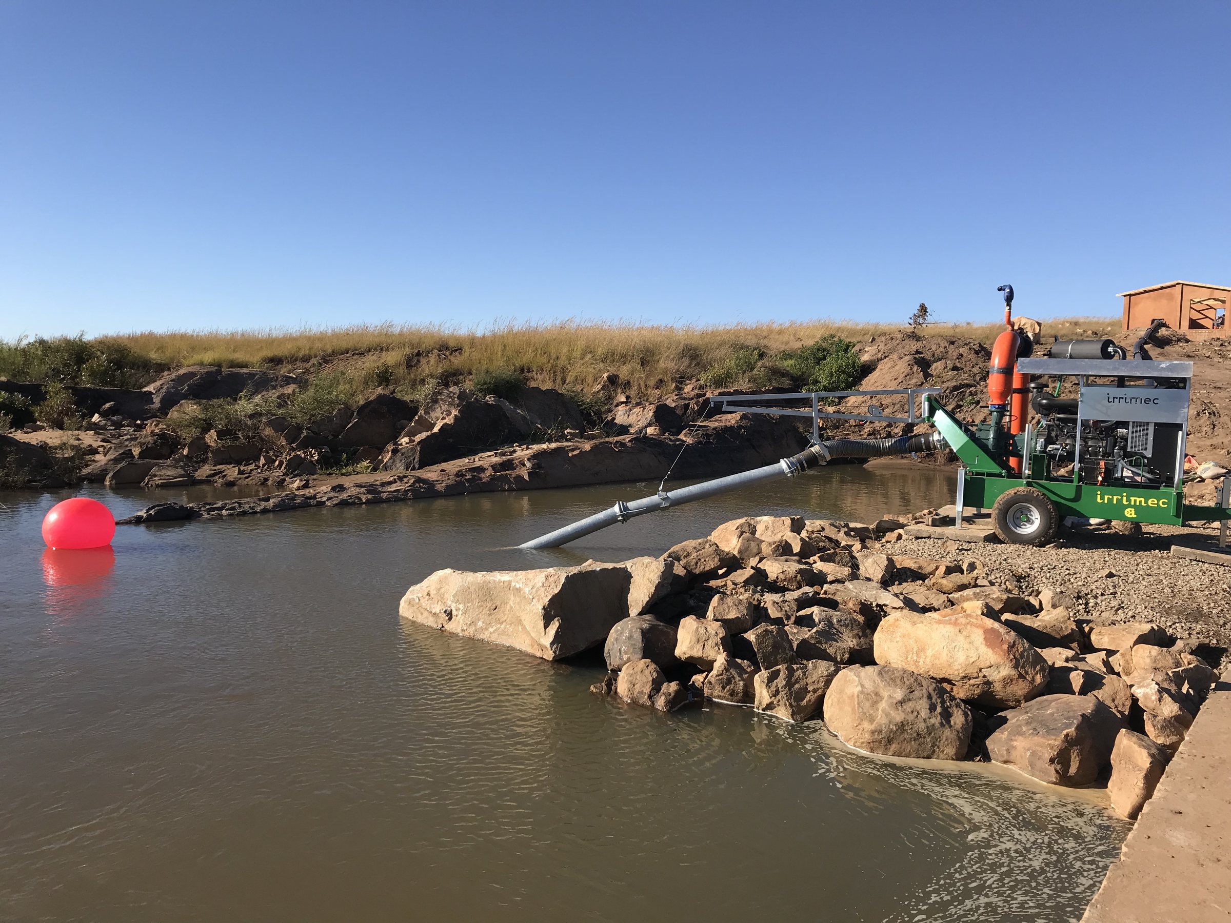 A trailer-mounted pump beside a rock-lined pool, drawing water through a suction pipe.