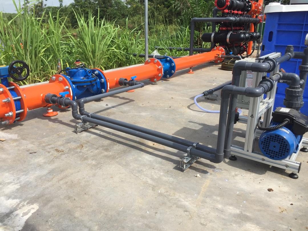 A station on a concrete slab: orange steel mainline, blue control valves, disc filters and a dosing pump.